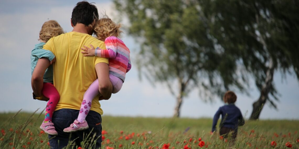 man carrying to girls on field of red petaled flower